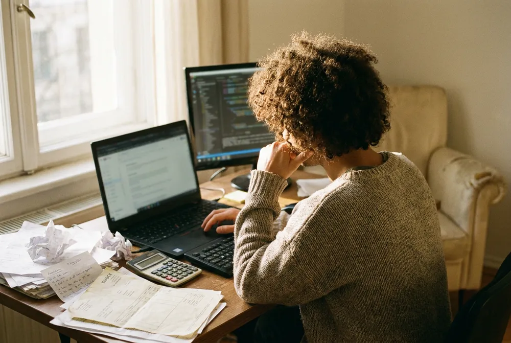 Persona trabajando en su escritorio con facturas y una calculadora junto a la laptop